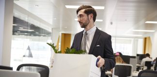 Fired male employee holding box of belongings in an office