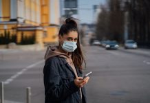 Girl in protective mask using smartphone outdoors. COVID 19. World coronavirus pandemic